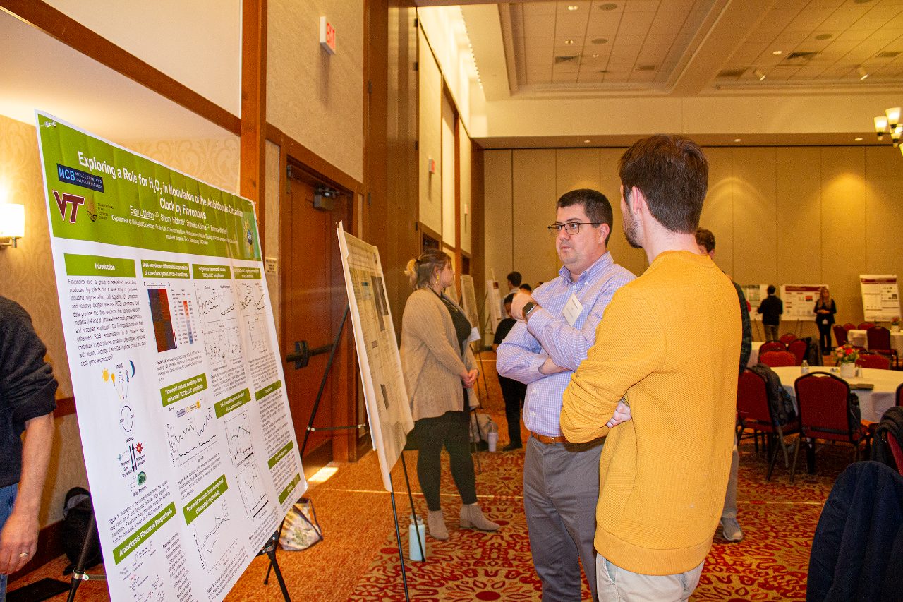 This shows a student explaining his research poster to a symposium attendee.